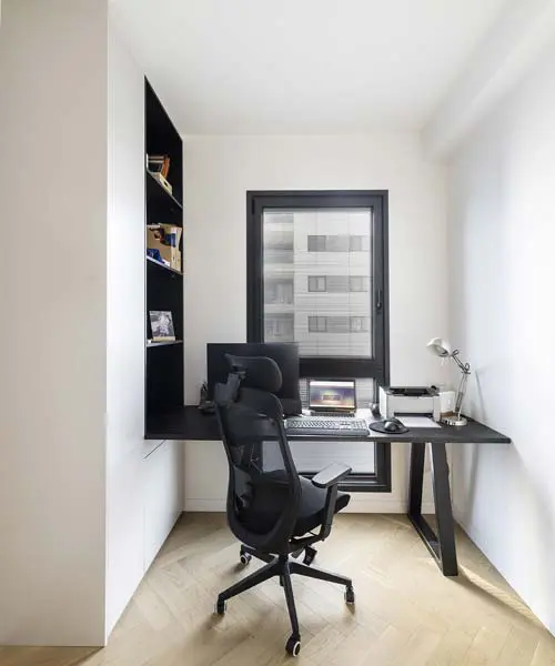 חדר עבודה מעוצב עם שולחן עבודה רחב וארוך, המשלב נגיעות אלגנטיות של שחור בגופי תאורה ובפרטי עיצוב שונים, ליצירת סביבה נוחה ויצירתית.