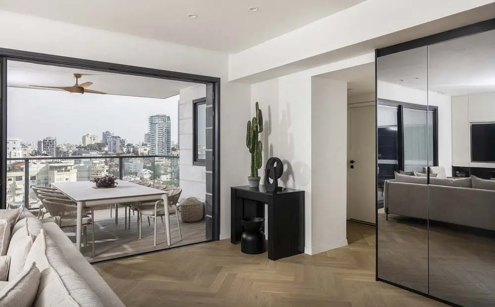 סלון מודרני מרווח בדירת קבלן 4 חדרים ברמת גן, עם יציאה ישירה למרפסת מקורה המציגה נוף אורבני של העיר