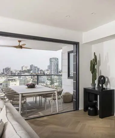 סלון מודרני מרווח בדירת קבלן 4 חדרים ברמת גן, עם יציאה ישירה למרפסת מקורה המציגה נוף אורבני של העיר