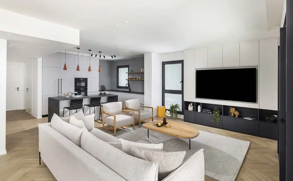 מבט רחב על החלל המרכזי בדירת בוטיק, המשלב בהרמוניה מטבח מודרני בגוונים כהים וסלון עם ארון טלוויזיה מעוצב ופתרונות אחסון חכמים