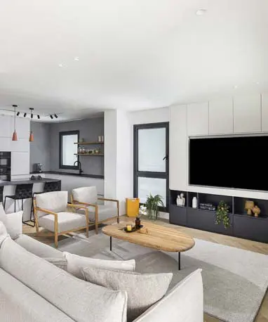 מבט רחב על החלל המרכזי בדירת בוטיק, המשלב בהרמוניה מטבח מודרני בגוונים כהים וסלון עם ארון טלוויזיה מעוצב ופתרונות אחסון חכמים