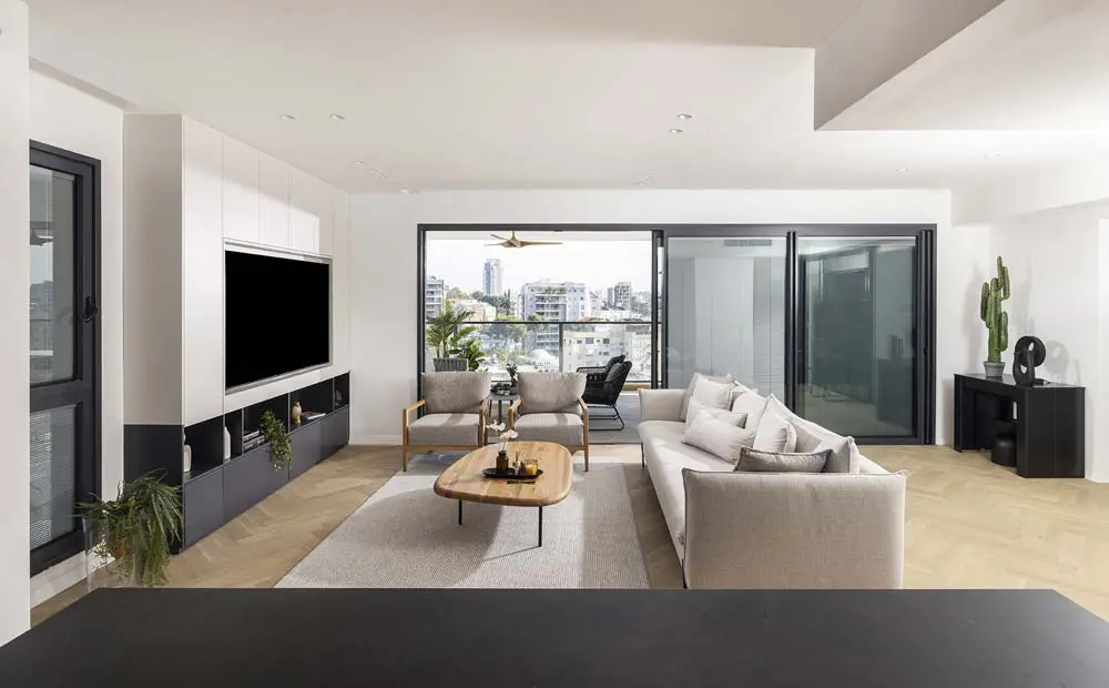 סלון יוקרתי בדירת 4 חדרים, המשלב עיצוב מודרני ונקי עם חלונות גדולים הנשקפים אל נוף אורבני עוצר נשימה של העיר ומגדליה.