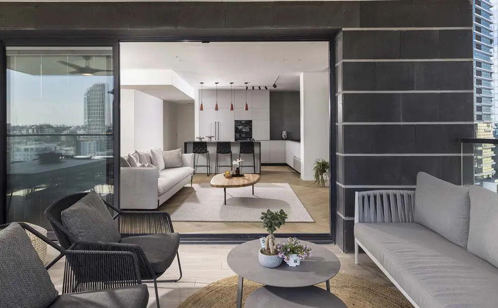 מבט מהמרפסת לתוך דירת 4 חדרים, המציג את החלל המרכזי הפתוח, שמאחד את המטבח המודרני, הסלון המעוצב והמרפסת המרווחת.