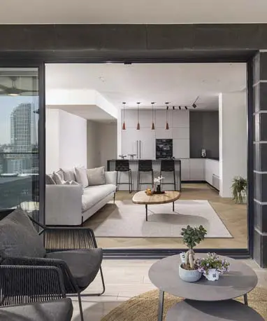 מבט מהמרפסת לתוך דירת 4 חדרים, המציג את החלל המרכזי הפתוח, שמאחד את המטבח המודרני, הסלון המעוצב והמרפסת המרווחת.