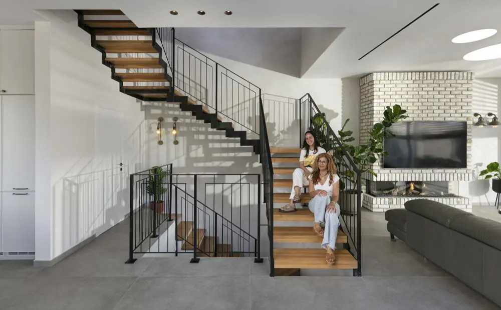 גרם מדרגות ברזל ועץ בחלל ציבורי עם קיר בריקים וקמין, כששתי המעצבות יושבות על המדרגות