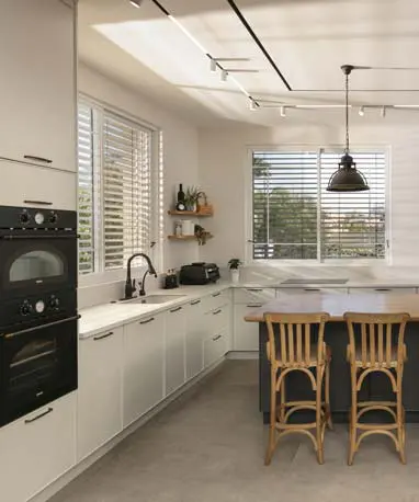 מטבח לבן עם אי גדול וכיסאות עץ, שילוב חזיתות חלקות ונישות עץ מוארות