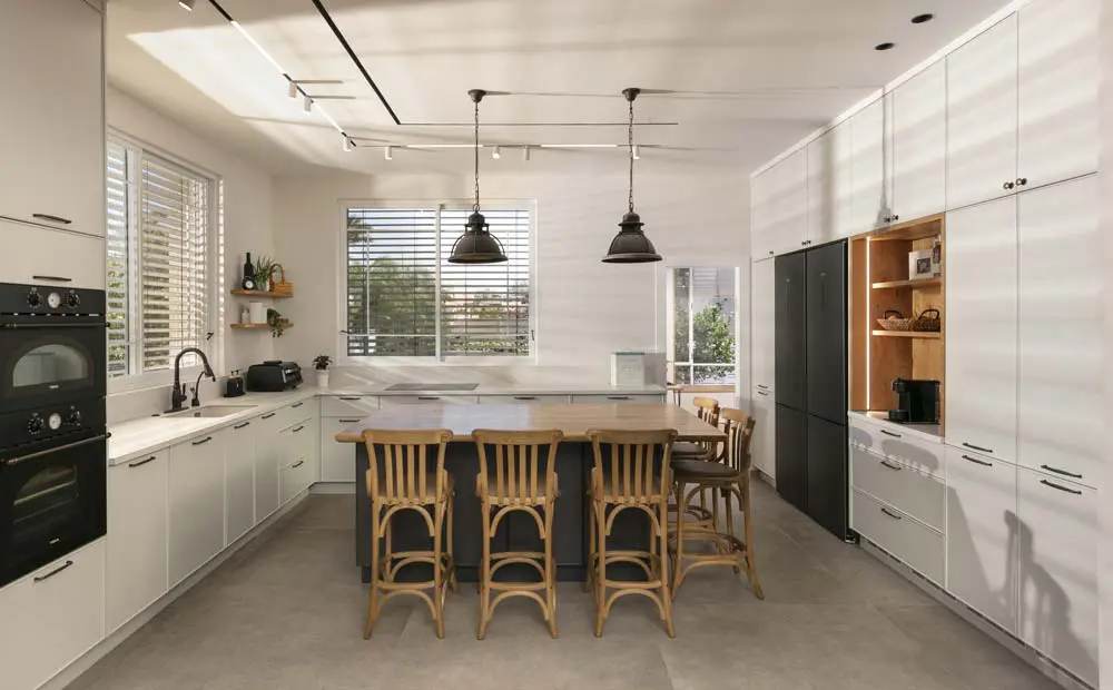 מטבח כפרי בהיר בצורת ר׳ עם אי מרכזי, כיסאות עץ ותאורה תלויה שחורה