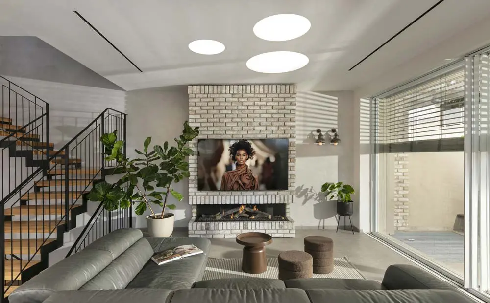 קיר טלוויזיה עם חיפוי בריקים וקמין מתחת למסך בסלון בית כפרי, עם יציאה רחבה לגינה