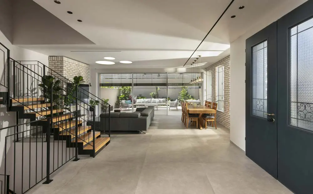 חלל כניסה פתוח בבית פרטי עם מדרגות ברזל ועץ, קירות בריקים והנמכות גבס עם פתחי מיזוג לינאריים