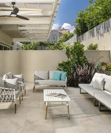 פינת ישיבה בגינה עם ריצוף בהיר ופרגולה, לצד קיר בריקים תואם לחזית הבית