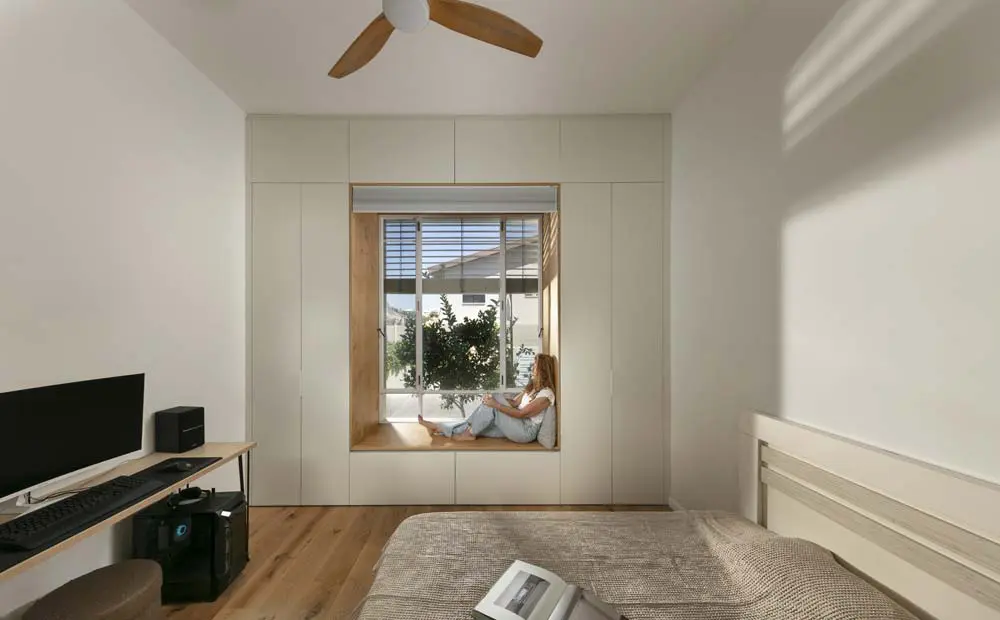 קיר ארונות מלא עם נישת חלון משולבת בעץ, המייצרת פינה אינטימית וישיבה טבעית מול האור