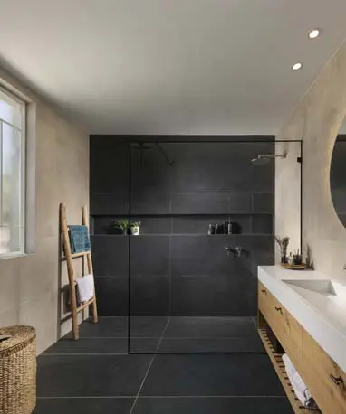 חדר אמבטיה הורים עם מראה עגולה מוארת, נגרות עץ וחיפוי כהה במקלחת