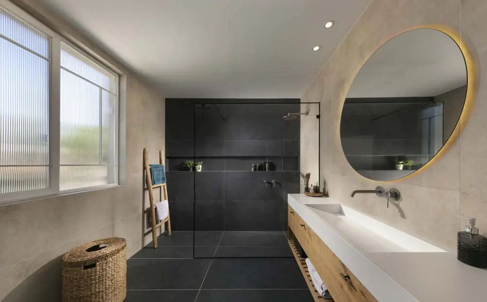 חדר רחצה הורים עם מקלחון זכוכית, אריחים כהים באזור הרחצה וארון עץ עם כיור כפול