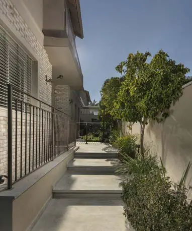 שביל ומדרגות בטון לצד חזית בית עם בריקים בהירים ומעקה מתכת שחור