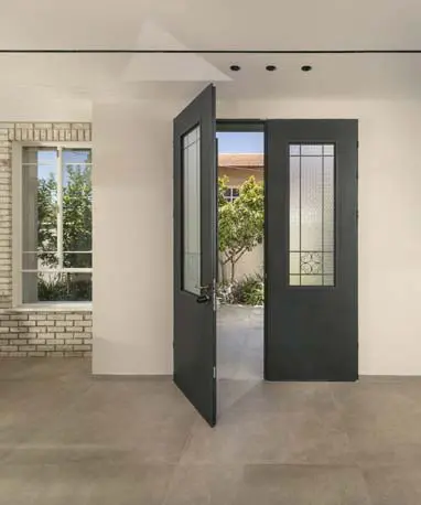 מבט מהבית אל הגינה דרך דלת עם זכוכית ופרזול כפרי, לצד חיפוי בריקים בהירים