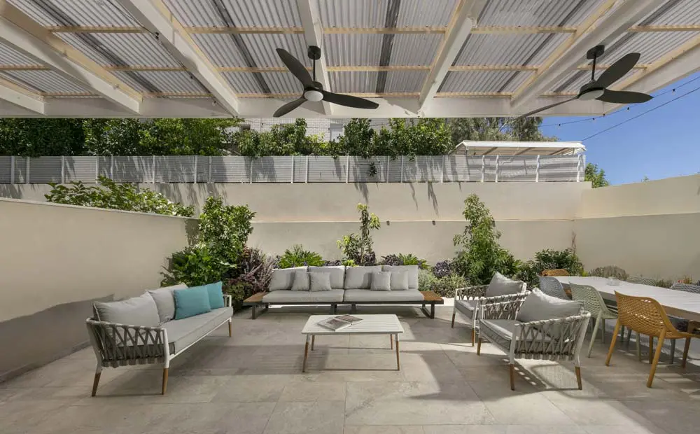 רחבת גינה מרוצפת עם פינת ישיבה חיצונית, פרגולה לבנה וקיר בריקים בהירים