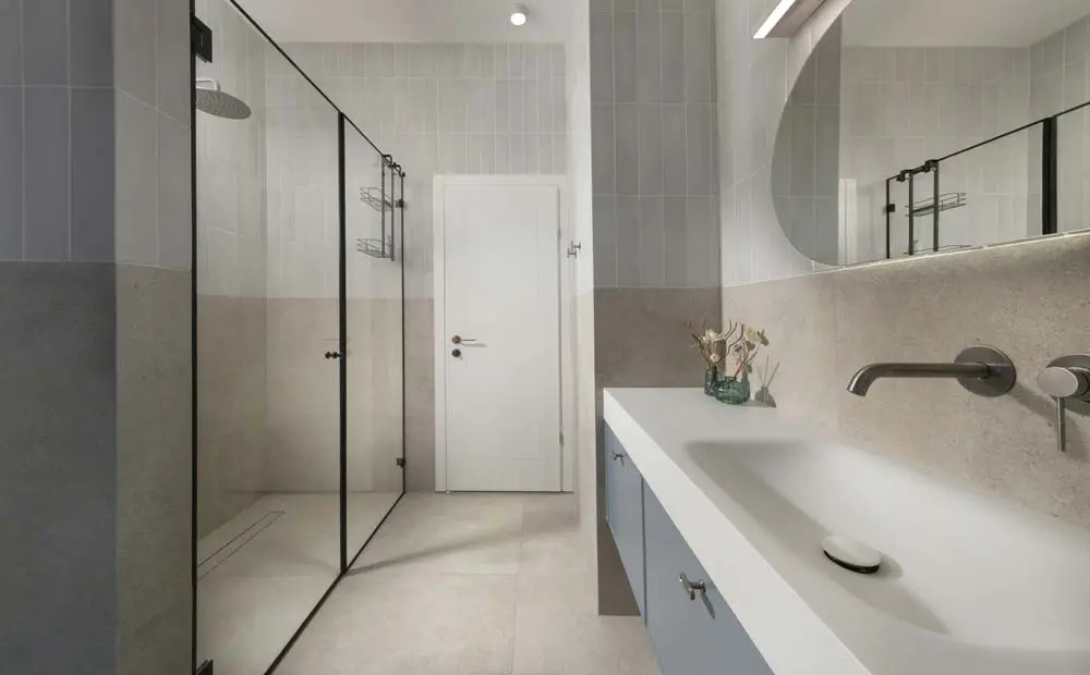 חדר רחצה כללי עם מקלחון זכוכית במסגרת שחורה, ארון כיור תכלת וחיפוי קיר דו־גוני