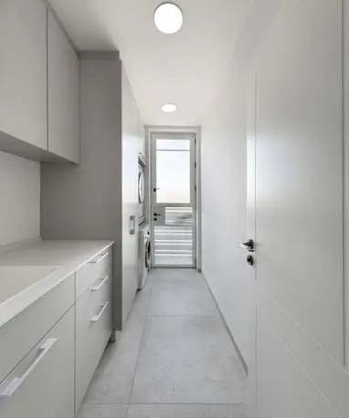 חדר כביסה עם אחסון מלא לאורך הקיר, מכונת כביסה מוערמת ודלת יציאה לחוץ