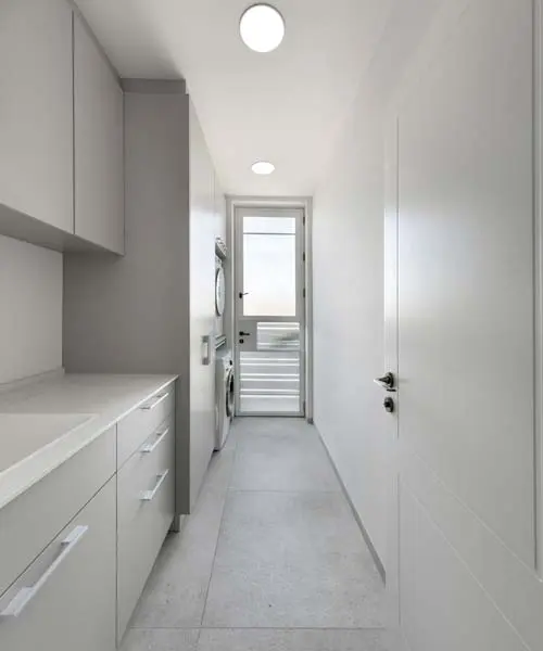 חדר שירות צר עם ארונות לבנים, משטח עבודה וכיור ומכונת כביסה ומייבש