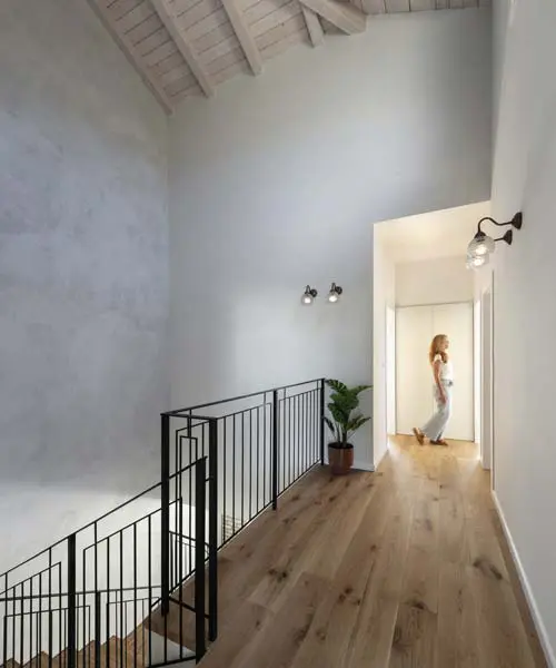 גלריה בקומה עליונה עם קורות עץ לבנות חשופות, רצפת עץ ומעקה ברזל שחור